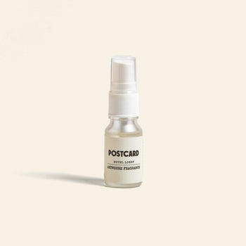 A 10ml Postcard Anywhere Fragrance in Hotel Lobby scent stands upright on a light beige background, capturing the luxury of hotel ambiance with this bestselling fragrance by Postcard.