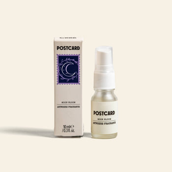 A 10ml Postcard Anywhere Fragrance in Moon Bloom sits next to its matching box with a crescent moon and star design, offering an enchanting, delicately scented aroma by Postcard.