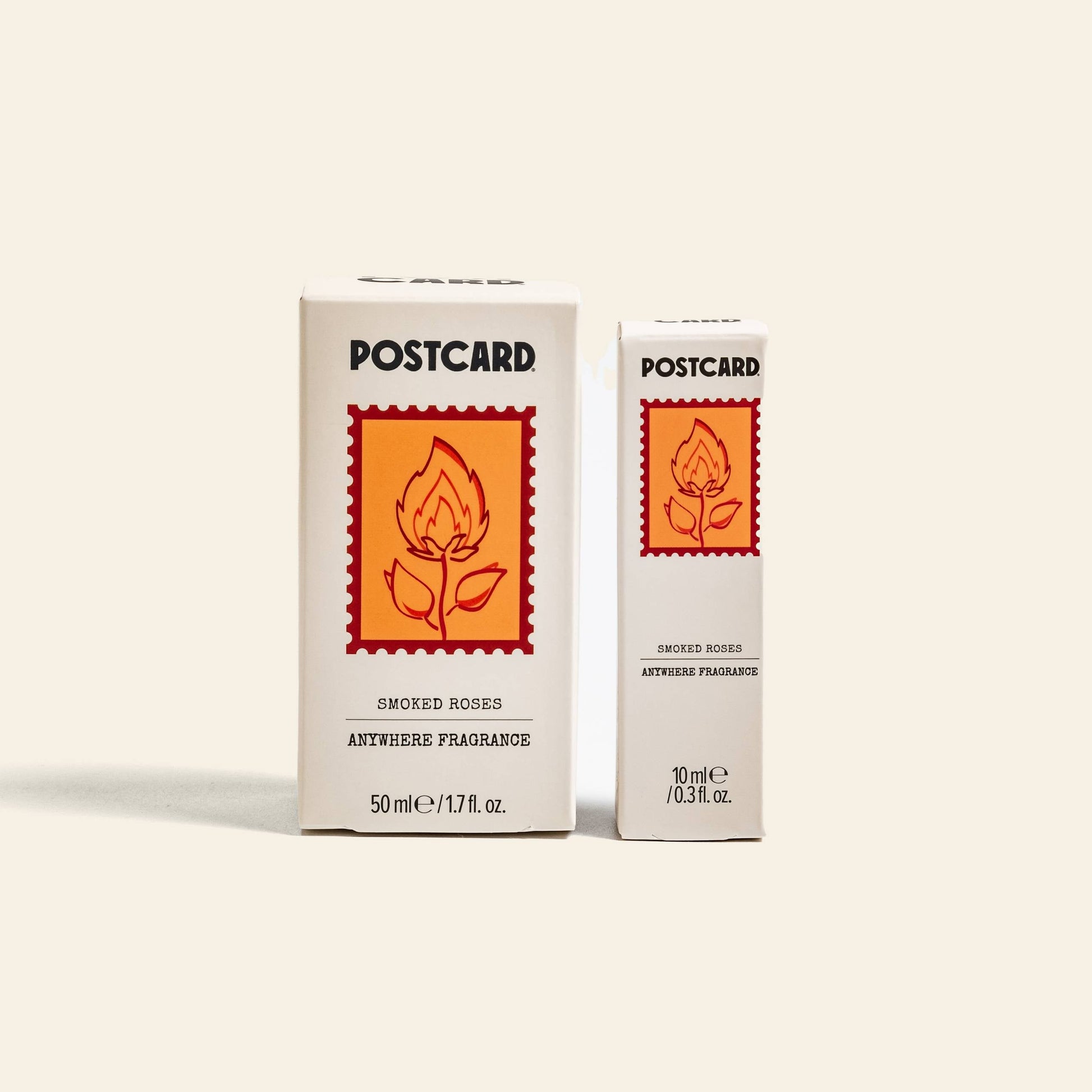 Two white boxes of Postcard Anywhere Fragrance, 50ml - Smoked Roses, display orange-red labels with a stylized rose and flame graphic, reflecting the fragrance’s rose perfume and amber scent notes inside.