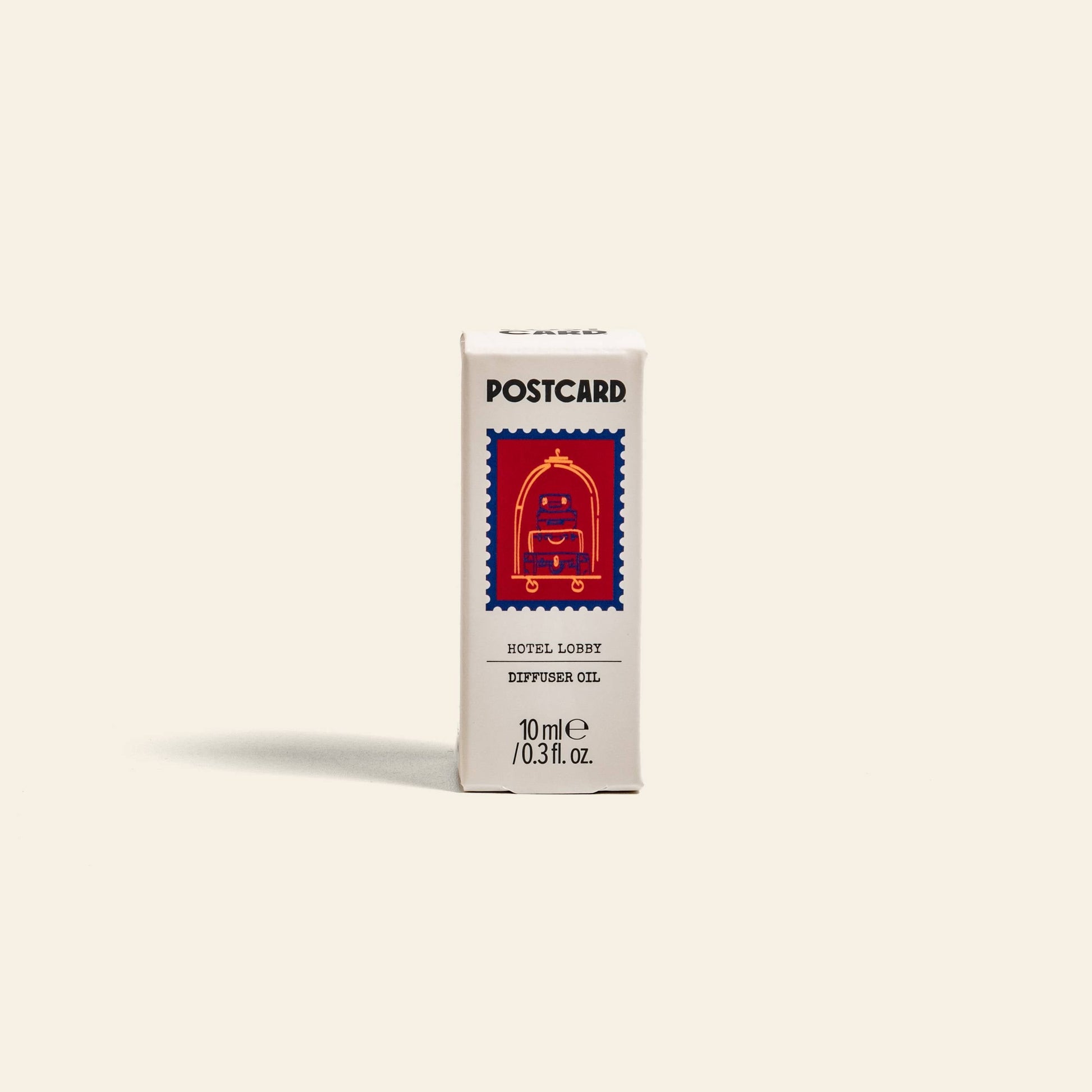 A small white Postcard box labeled Postcard Diffuser Oil, 10g - Hotel Lobby features a red bellhop cart illustration, evoking hotel luxury and a 5-star vibe against a plain beige background. Brand: Postcard.