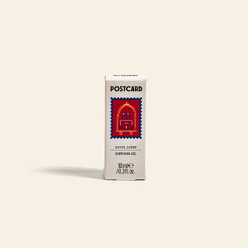 A small white Postcard box labeled Postcard Diffuser Oil, 10g - Hotel Lobby features a red bellhop cart illustration, evoking hotel luxury and a 5-star vibe against a plain beige background. Brand: Postcard.