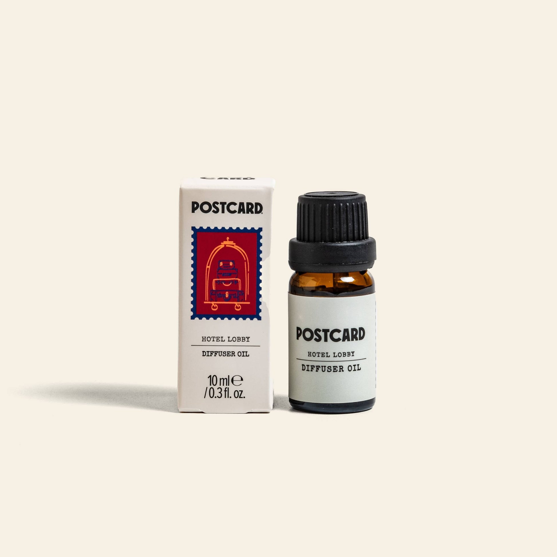 A 10g bottle of Postcard Diffuser Oil by Postcard stands beside its white box, which features a red postage stamp illustration. This luxe blend captures the essence of Hotel Lobby luxury in every drop.