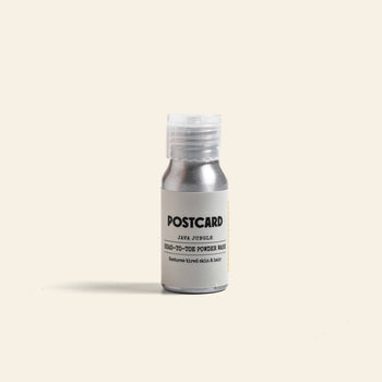 A small silver bottle of Postcard Head-To-Toe Powder Wash, 25g - Java Jungle, stands upright on a light beige background with a white cap; this sulfate-free powder wash features Stinging Nettle and is branded Postcard.