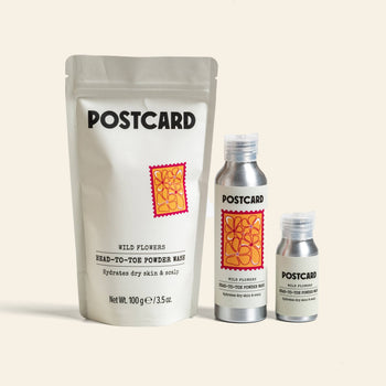 Three Postcard Head-To-Toe Powder Wash (80g, Wild Flowers) products—a large resealable pouch and two metallic bottles—showcase the sulfate-free, powder-to-foam cleanser by Postcard, arranged on a neutral background.
