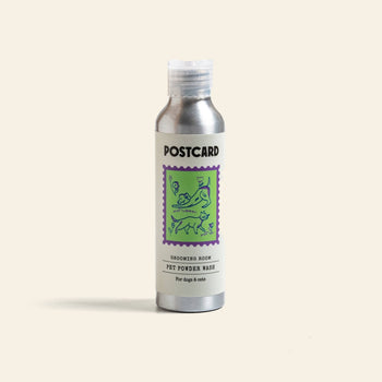 A silver Postcard PET Powder Wash bottle (80g) features a purple and green dog-and-cat illustration. Labeled Grooming Room, it’s a sulfate-free powder-to-foam cleanser for dogs & cats, shown upright against a plain background.