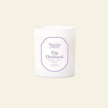 The Reminds Me Of Fig Orchard Candle, 10oz by Reminds Me Of features fig leaves, freesia, and bamboo notes in a frosted glass jar with a white candle, shown against a plain beige background.