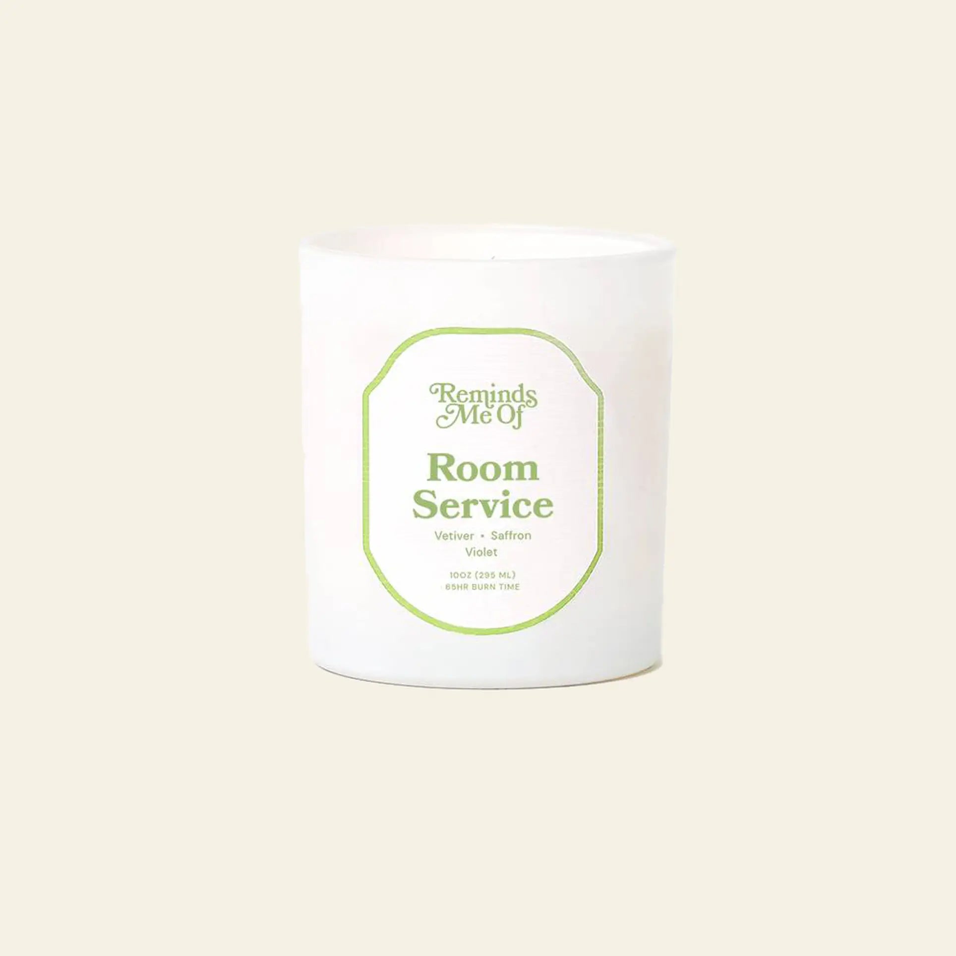 A 10oz Reminds Me Of Room Service Candle by Reminds Me Of, in a simple glass jar with soothing vetiver and violet notes, is displayed against a plain beige background.