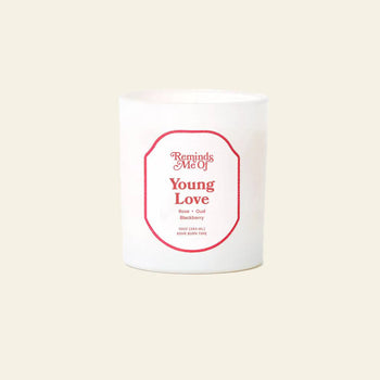 The Reminds Me Of Young Love Candle, 10oz by Reminds Me Of is a white candle in a glass jar with a red label. Scented with rose petals, oud, and blackberry. Light beige background and features the tagline Burn Every Time.