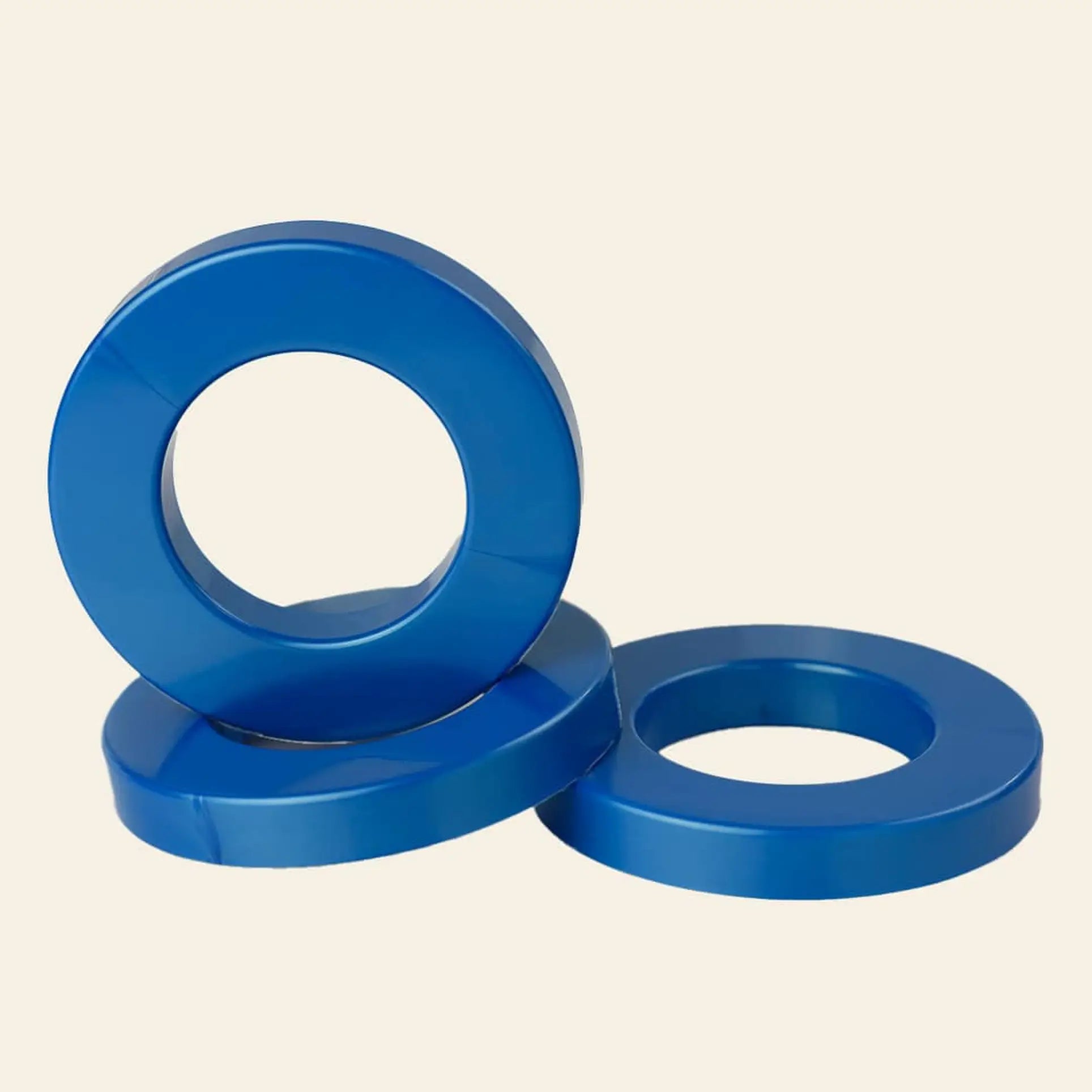 Three vibrant blue metal Ring A Date Calendar Rings by Ring-A-Date are stacked on a light beige background—ideal for personalizing your calendar or adding flair to your Ring-A-Date wall calendar.
