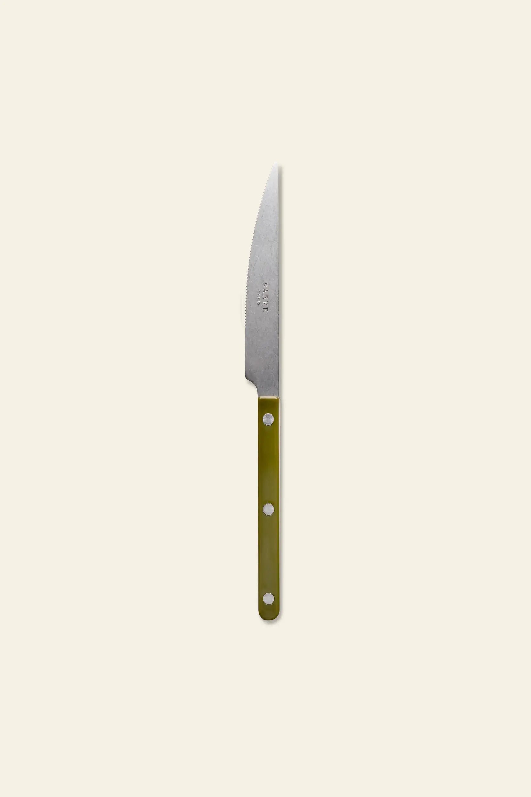 The Sabre Bistrot Vintage Dinner Knife by Sabre features a pointed stainless steel blade and a green handle with three silver rivets, inspired by French bistrot style and shown on a light beige background.