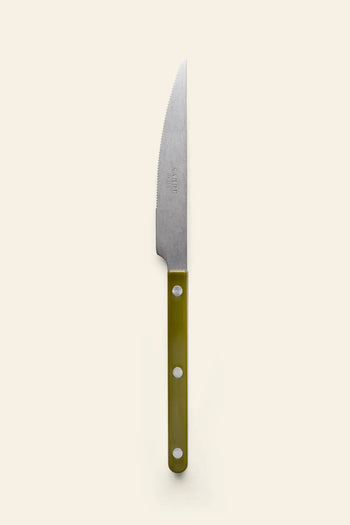 The Sabre Bistrot Vintage Dinner Knife by Sabre features a silver serrated blade and an olive green handle with three rivets, reflecting French bistrot style, shown on a plain light beige background.
