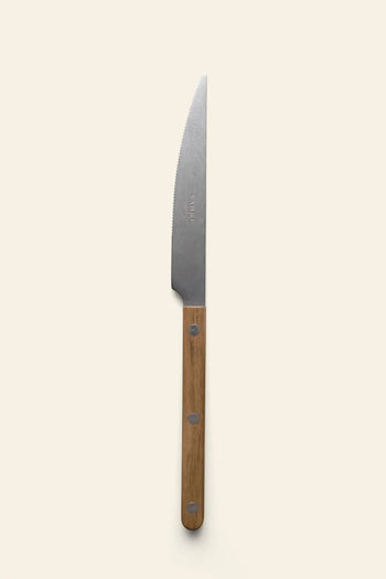 The Sabre Bistrot Vintage Dinner Knife by Sabre, featuring a serrated blade and wood handle with three metal rivets, stands vertically on a plain light beige background, reflecting classic French bistrot style.