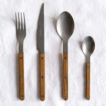 The Sabre Bistrot Vintage Dinner Knife by Sabre, featuring a metal blade and wooden handle, is arranged on a white fabric backdrop for a charming French bistrot style.