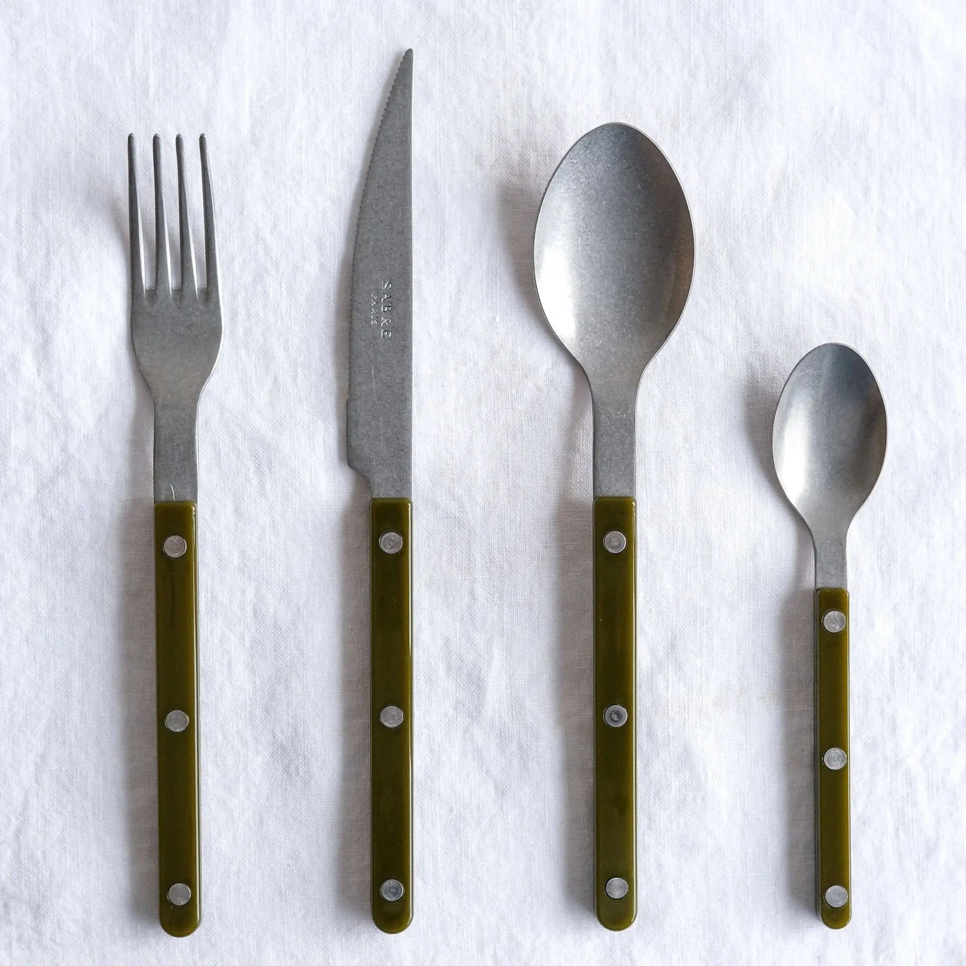 The Sabre Bistrot Vintage Soup Spoon by Sabre, featuring a green handle and metal rivets, is displayed on a white cloth backdrop, channeling the charm of a French café.