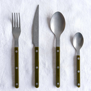 The Sabre Bistrot Vintage Soup Spoon by Sabre, featuring a green handle and metal rivets, is displayed on a white cloth backdrop, channeling the charm of a French café.