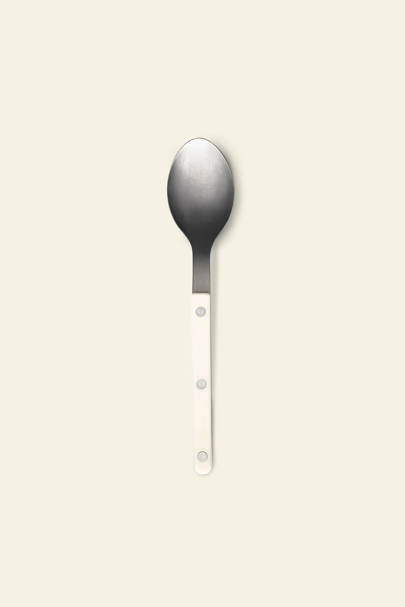 The Sabre Bistrot Vintage Soup Spoon by Sabre features a white handle with three silver rivets and a stainless steel bowl, evoking classic French cafe style, displayed on a simple light beige background.