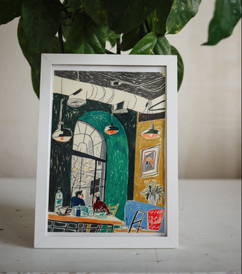 A framed print by Sarah Mari Shaboyan, Cozy Interior at Eat & Fit Caffe, Yerevan, Armenia, features a couple enjoying breakfast at a café table beneath hanging lights, with green arched windows and plants in the background.