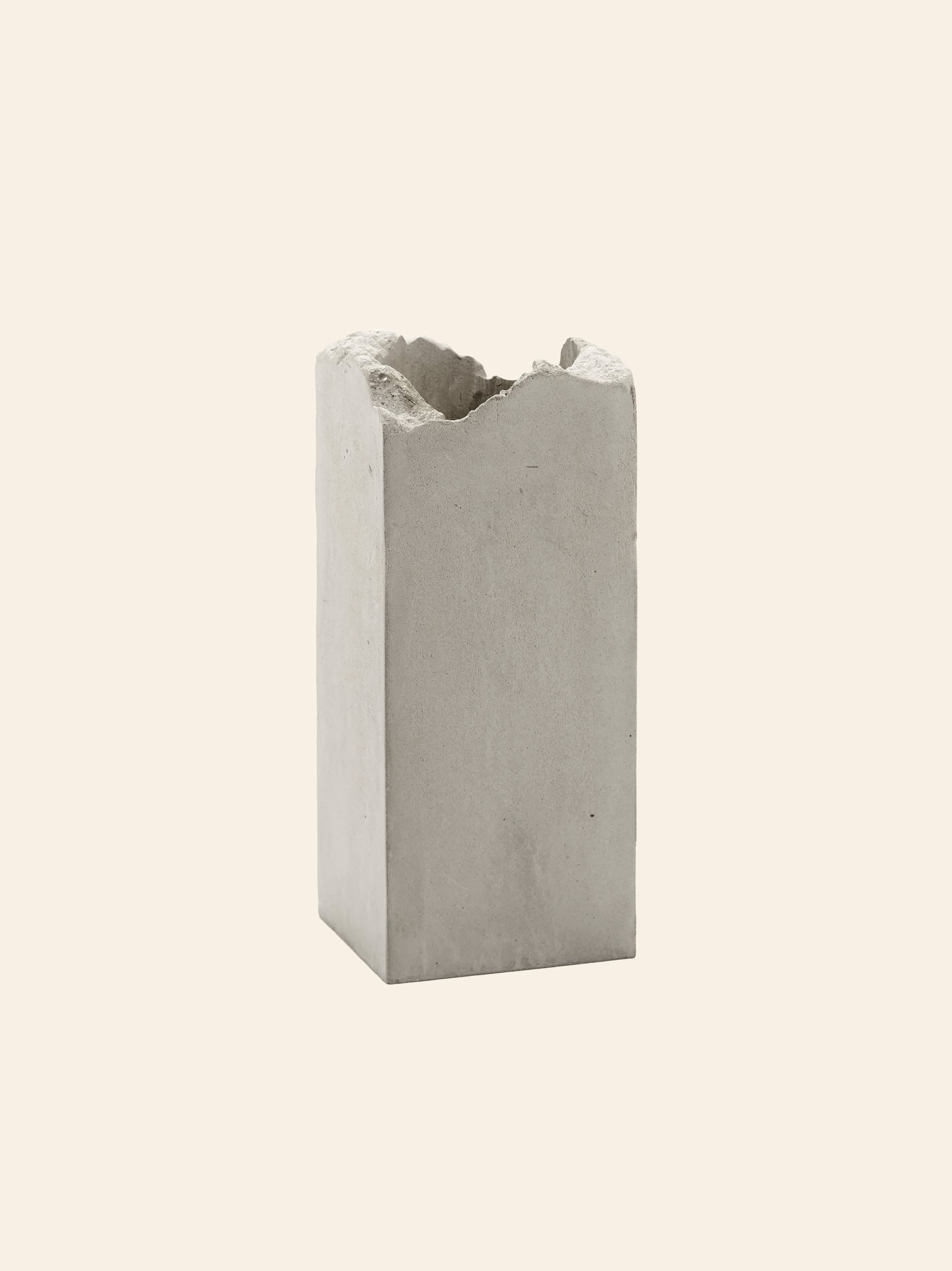 The Serax Broquaine Concrete Vase S - Grey by Serax stands upright with a rough, uneven top edge against a plain beige background—a striking example of modern design.