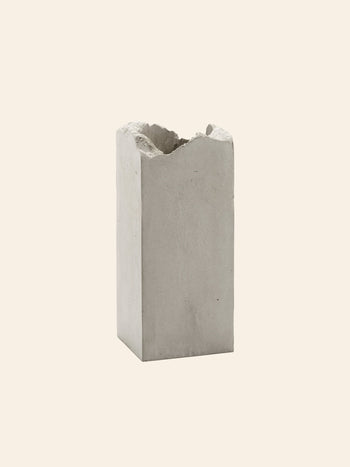 The Serax Broquaine Concrete Vase S - Grey by Serax stands upright with a rough, uneven top edge against a plain beige background—a striking example of modern design.
