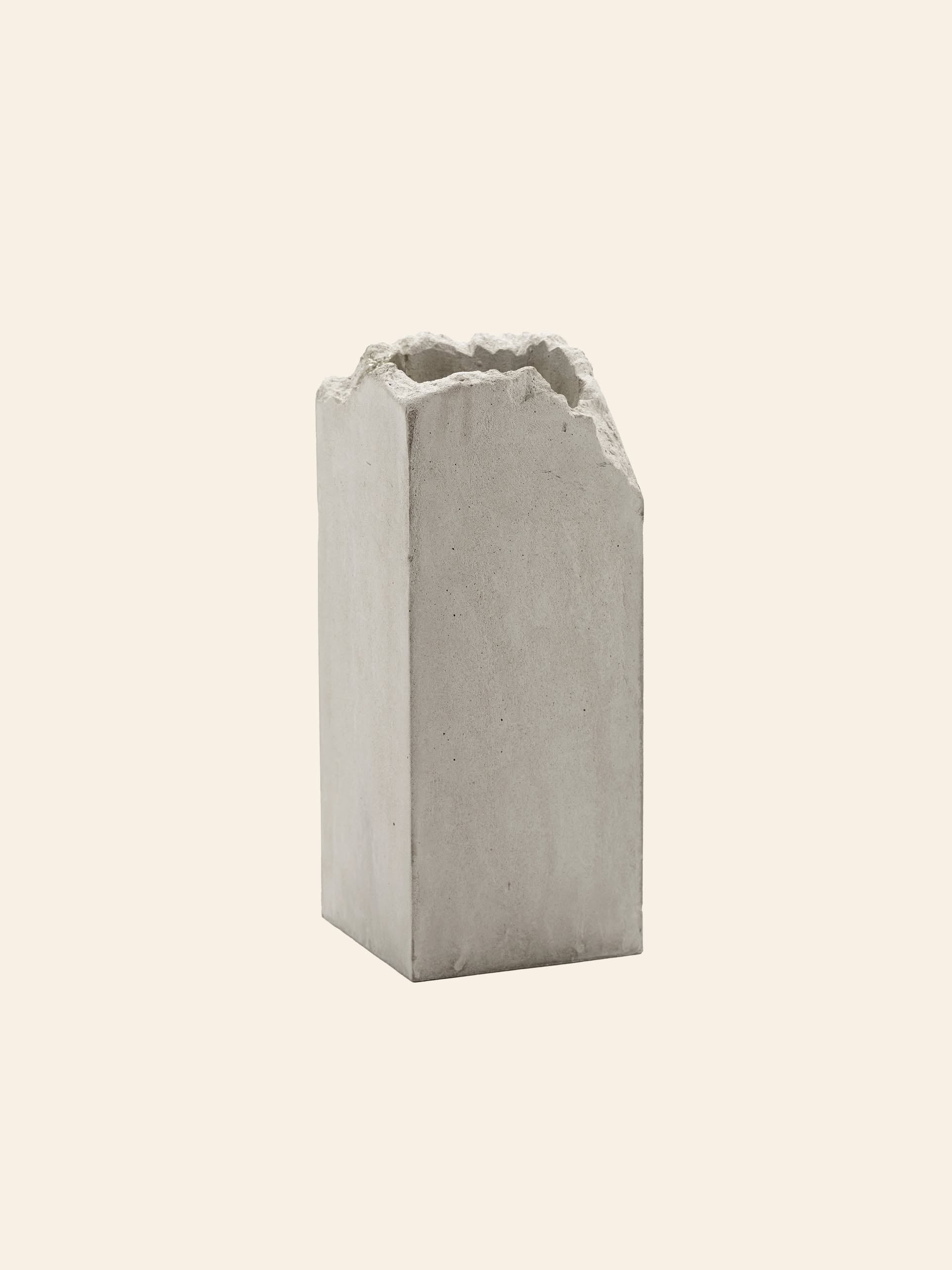 The Serax Broquaine Concrete Vase S in grey by Serax stands upright with its rough, jagged top edges against a plain light beige background, showcasing modern artistry.