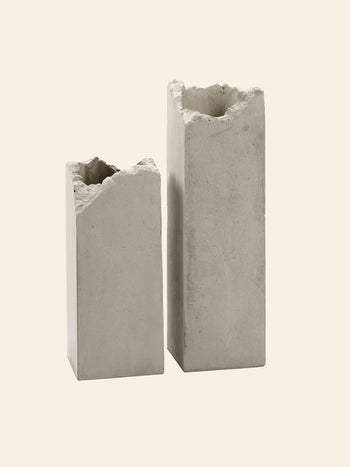 Two tall Serax Broquaine Concrete Vases S in grey, with rough, uneven tops, stand side by side against a beige background, showcasing Serax’s modern artistry.
