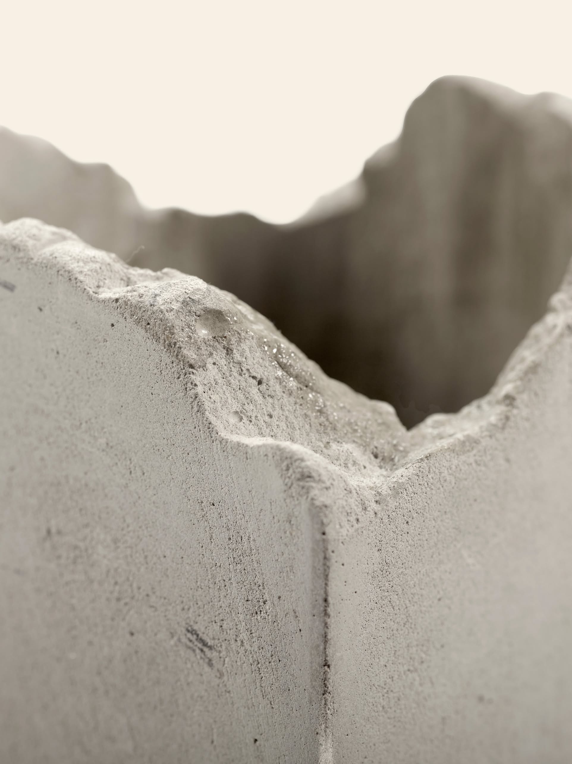 Close-up of the rough, jagged edge of the Serax Broquaine Concrete Vase S in grey by Serax, featuring an irregular wavy surface texture with an out-of-focus background, reminiscent of Patrick Pariss modern artistry.
