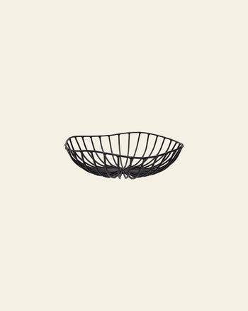 The Serax Catu Bread Basket L - Black, by Serax, is a shallow, oval metal basket with an open artistic design, displayed against a plain light beige background.
