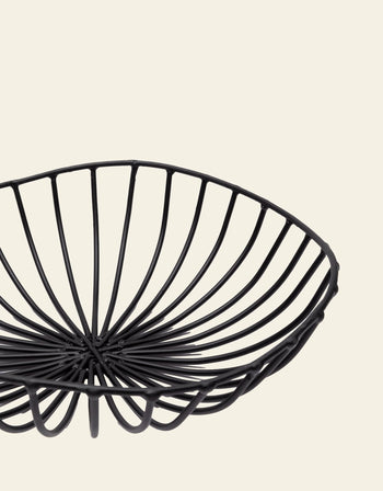 The Serax Catu Bread Basket L - Black by Serax features a round, modern design with evenly spaced metal bars curving upward, set against a plain light beige background.