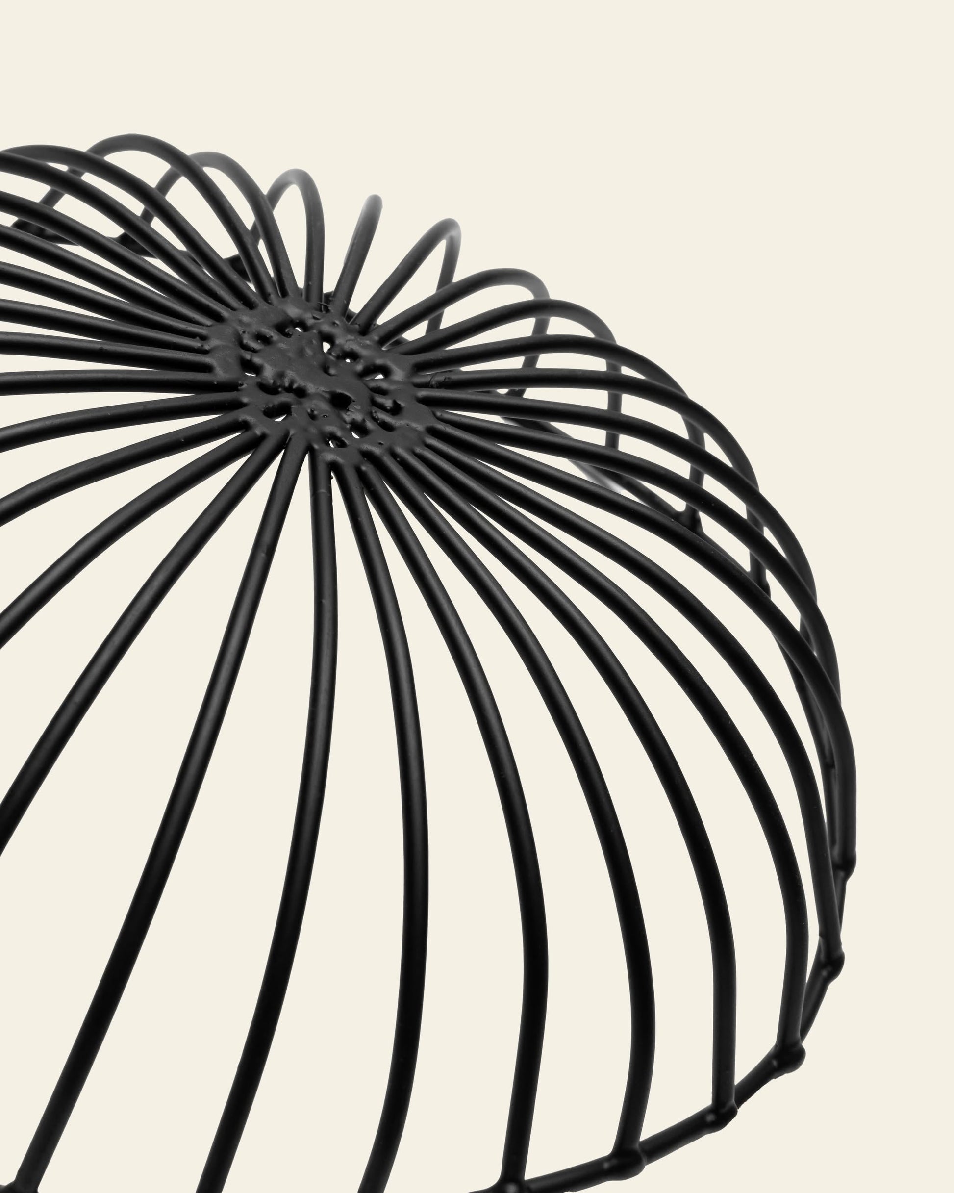 Close-up of the Serax Catu Bread Basket L in black by Serax. This wire, dome-shaped piece features an artistic, outward-curving design against a plain light beige background, evoking minimalist elegance.