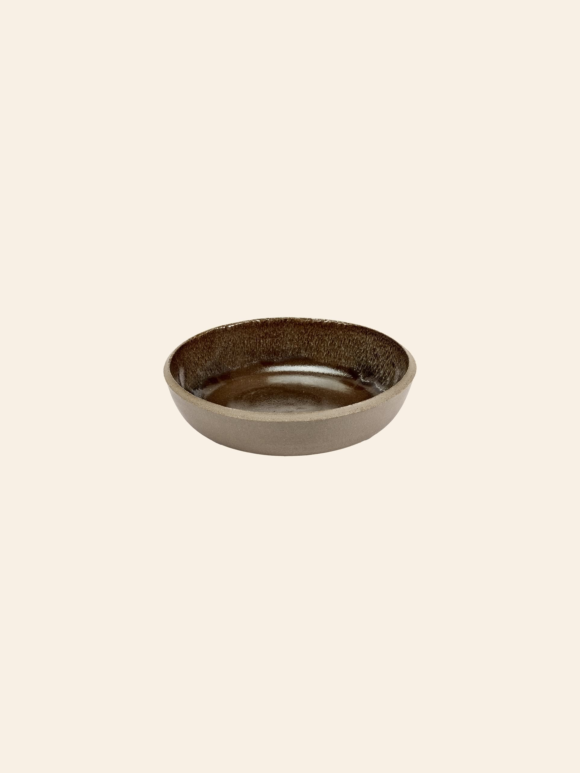 The Serax Fck Deep Plate in grey by Serax features a shallow, round ceramic stoneware design with a subtly textured surface, set against a plain light beige background that reflects the raw elegance of brutalist architecture.