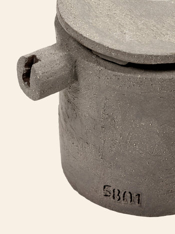 A close-up of the Serax Fck Teapot N°3 - Grey Brown by Serax shows its round, concrete form with lid and protruding handle, stamped “5801” near the base. The urban ceramics design stands out against a plain light background.