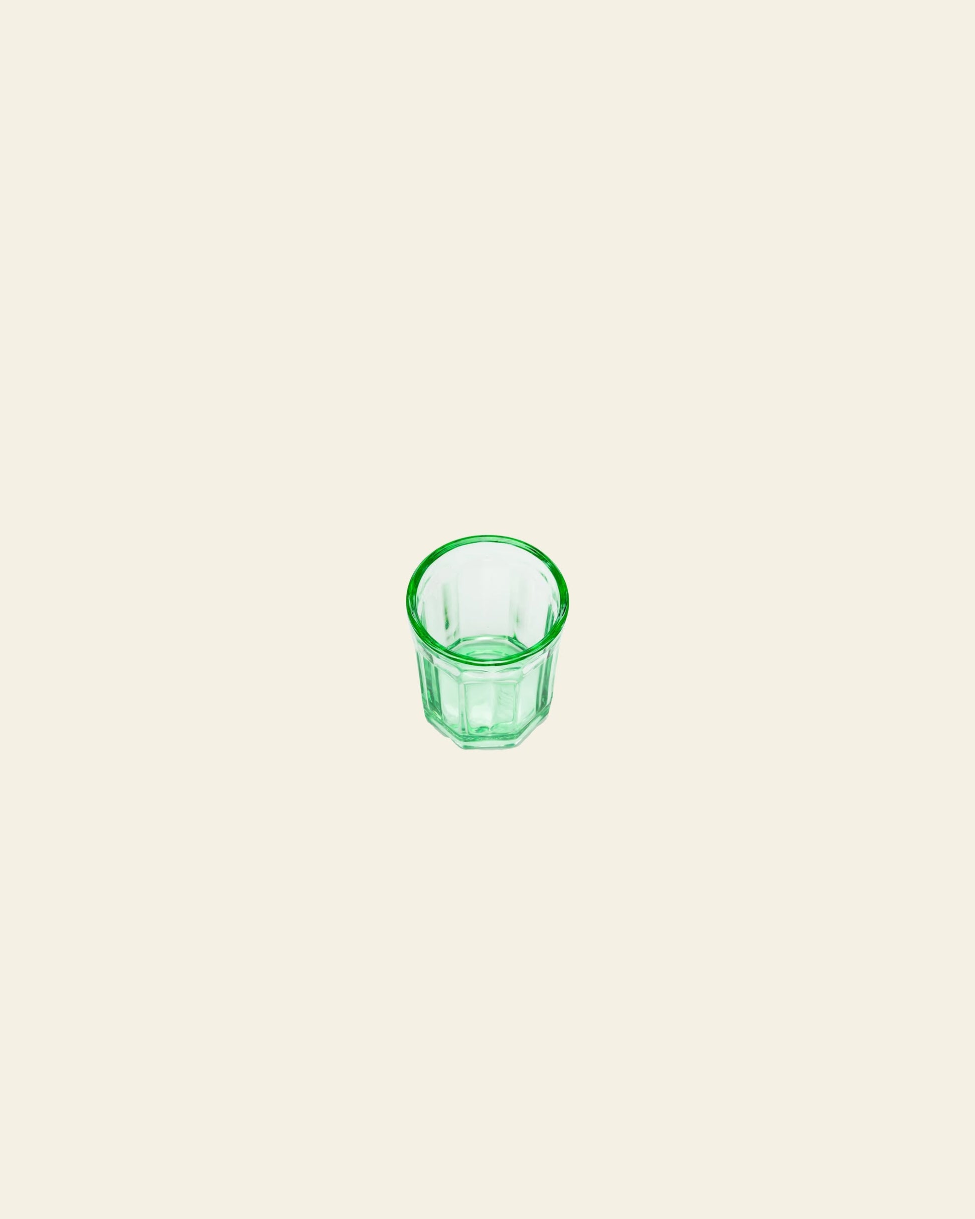 A medium-sized green glass from the Serax Fish & Fish Glass M collection by Serax, featuring a faceted design, is centered on a plain off-white background.