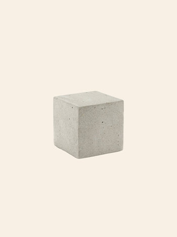The Serax Marie Cube Concrete in grey by Serax rests on a light beige background, its smooth finish and clean lines offering an industrial accent—ideal for contemporary decor.