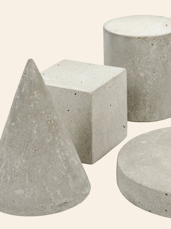 The Serax Marie Cube Concrete - Grey by Serax features a slightly rough texture and industrial feel, making it an ideal modern decor piece when styled with other geometric shapes on a light beige background.