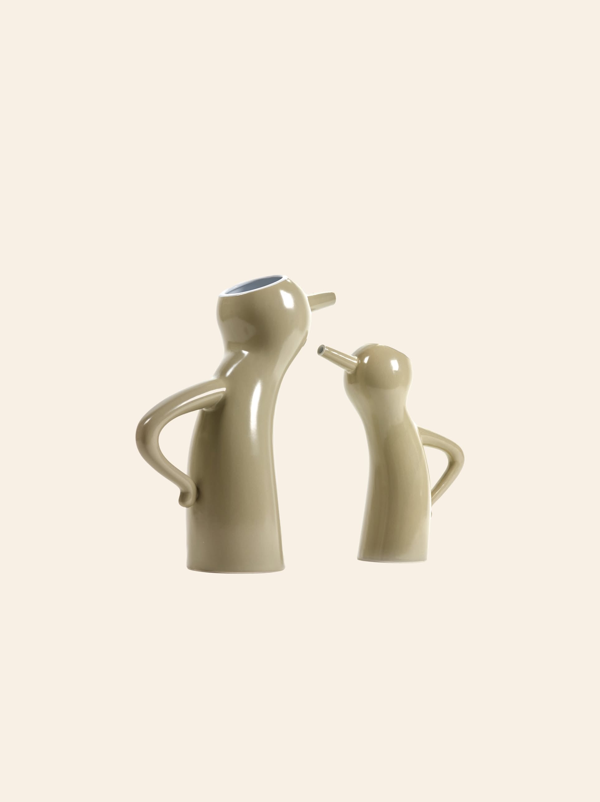Two taupe Serax Monsieur Cruchot Jug L ceramics, featuring arm-like handles and nose-shaped spouts, stand face to face hands-on-hips style, serving as versatile decorative pieces by Serax against a plain background.