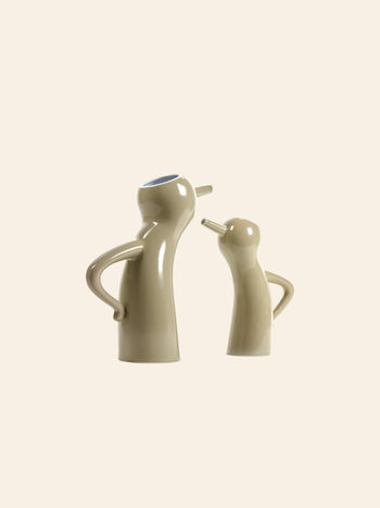 Two taupe Serax Monsieur Cruchot Jug L ceramics, featuring arm-like handles and nose-shaped spouts, stand face to face hands-on-hips style, serving as versatile decorative pieces by Serax against a plain background.