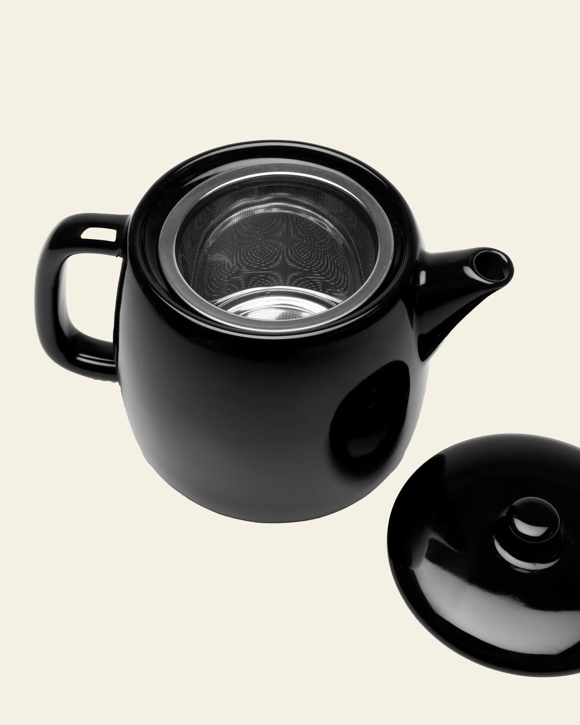 The Serax Passe-Partout Teapot in black by Serax is shown with its lid set aside and metal infuser visible, highlighting its minimalist design against a plain light background.