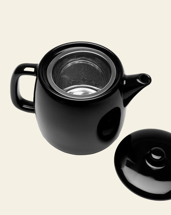 The Serax Passe-Partout Teapot in black by Serax is shown with its lid set aside and metal infuser visible, highlighting its minimalist design against a plain light background.