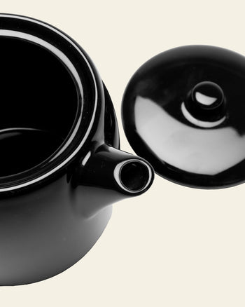 The Serax Passe-Partout Teapot - Black by Serax is shown with its lid off, highlighting the open top and spout. Its minimalist black porcelain design stands out against a plain, light background.