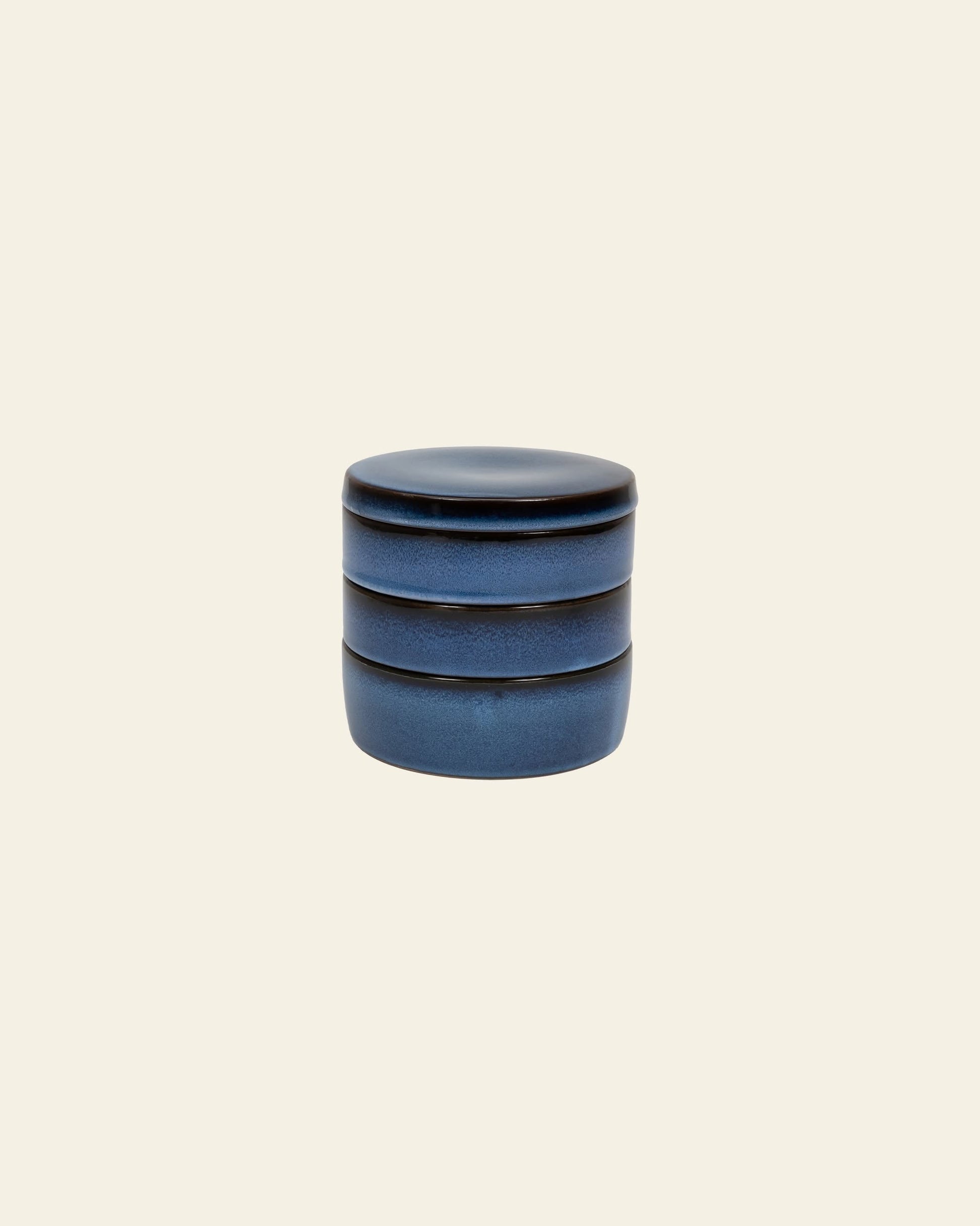 The Serax Pure Stackable Bowl S, Set of 3 in matte dark blue handcrafted stoneware by Serax features three cylindrical tiers with a matching lid, shown against a plain light beige background.