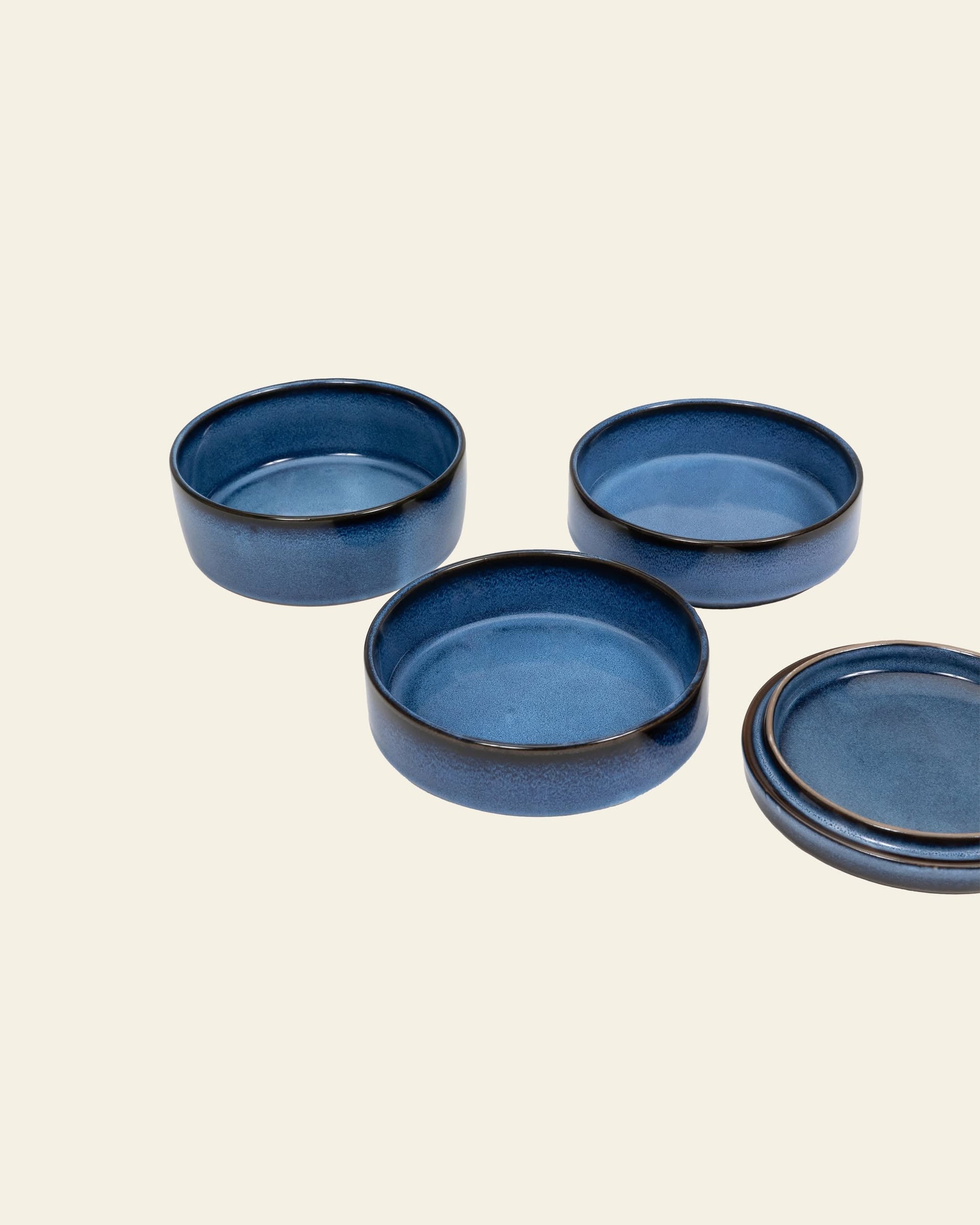 Three round, dark blue Serax Pure Stackable Bowl S by Serax are arranged on a light beige background, with two upright and one upside down to show the earthy glaze.