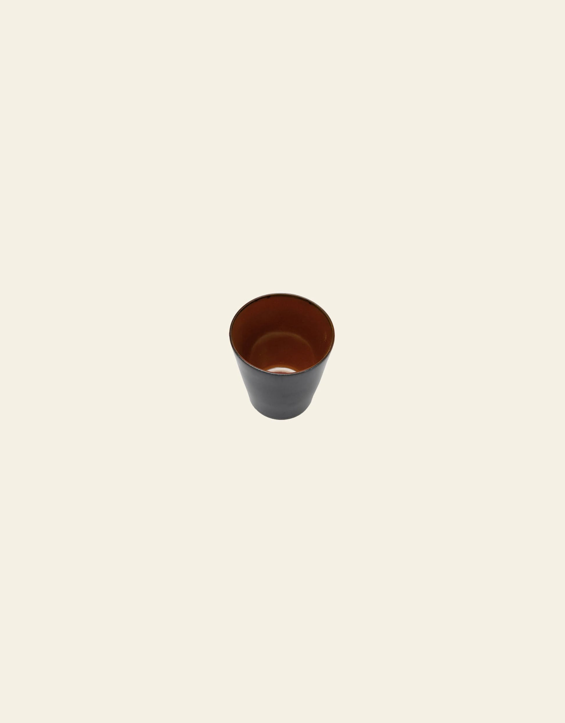 The Serax Terres De Rêves Conical Cup M features a dark brown exterior and reddish-brown interior with a handcrafted glaze, displayed on a plain light beige background.