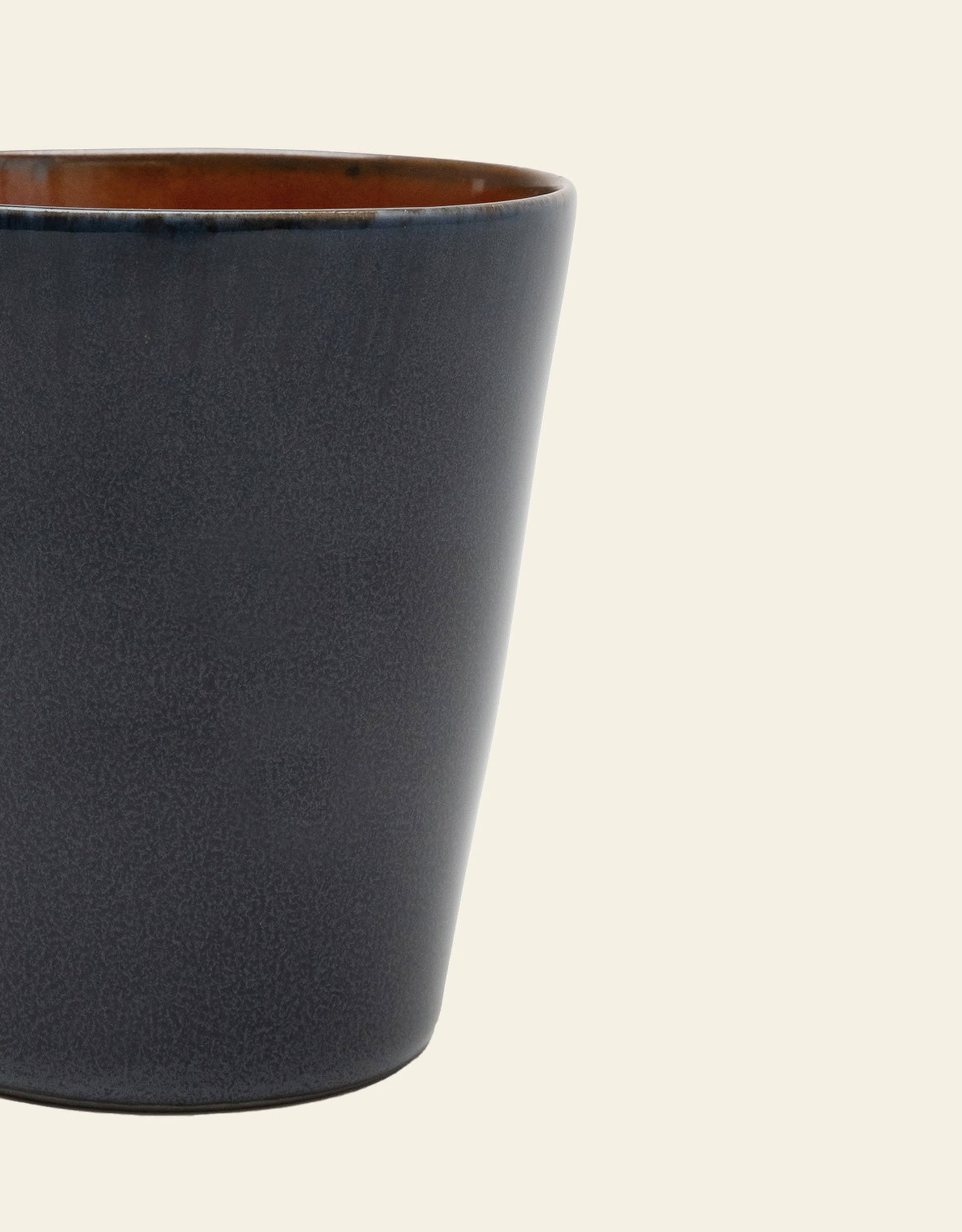 The Serax Terres De Rêves Conical Cup M by Serax is a handcrafted, dark gray ceramic cup with a slightly flared rim, shown against a plain off-white background.