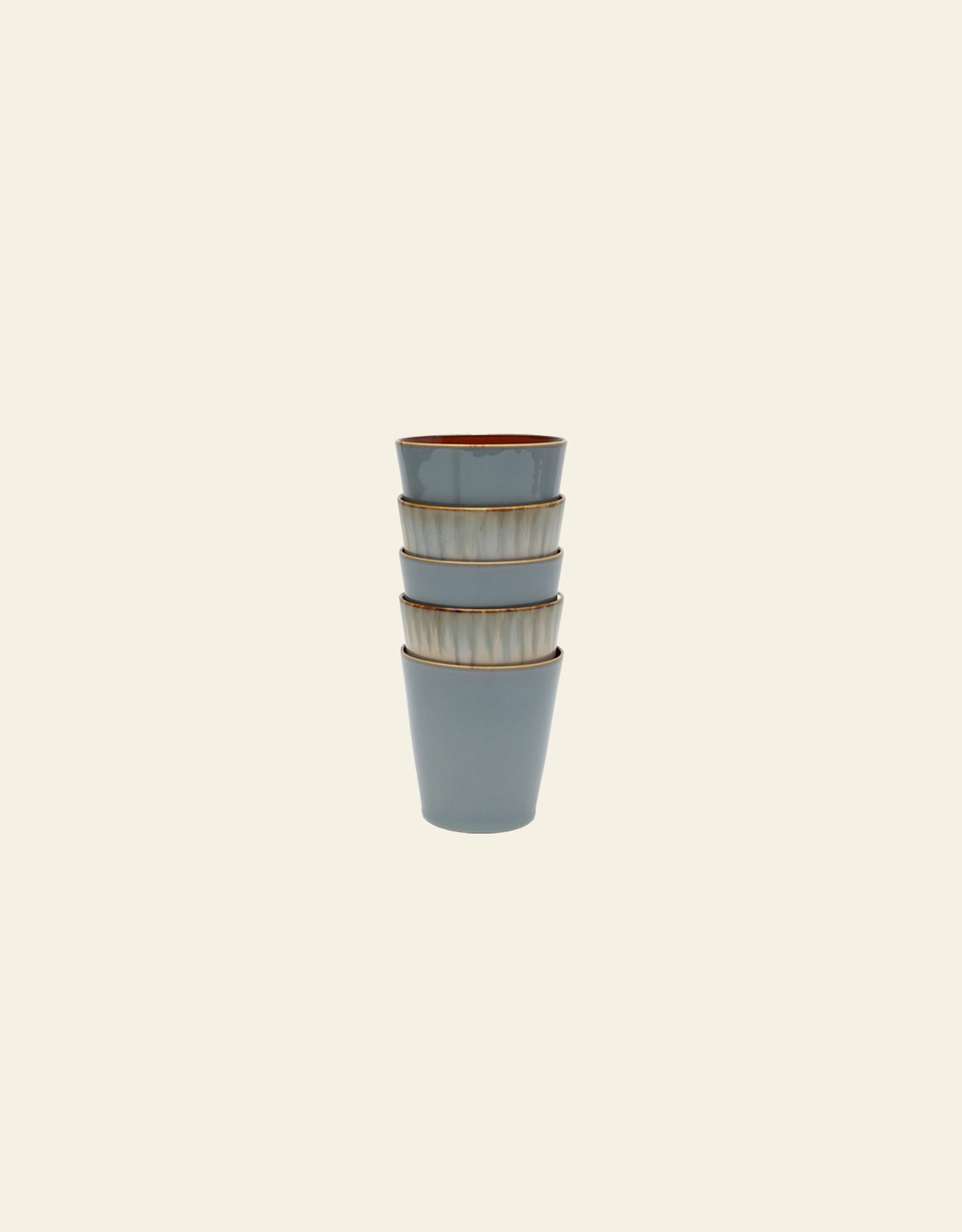 Four Serax Terres De Rêves Conical Cup M by Serax, in muted blue with brown rims and a handcrafted glaze, are stacked vertically against a plain light background.