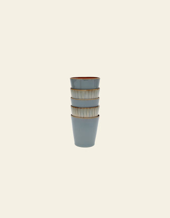 Four Serax Terres De Rêves Conical Cup M by Serax, in muted blue with brown rims and a handcrafted glaze, are stacked vertically against a plain light background.