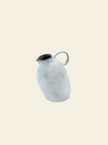 The Serax Terres De Rêves Jug °1 - White by Serax features a light gray finish, rounded and slightly asymmetrical body, and curved handle, creating an eye-catching statement piece against a plain off-white background.
