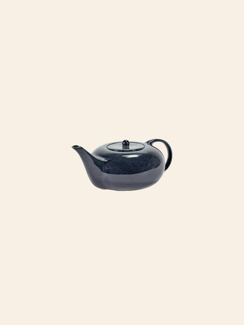 The Serax Terres De Rêves Teapot by Serax features a glossy dark blue rounded body, short spout, and small curved handle—an elegant tableware piece—presented against a plain light beige background.