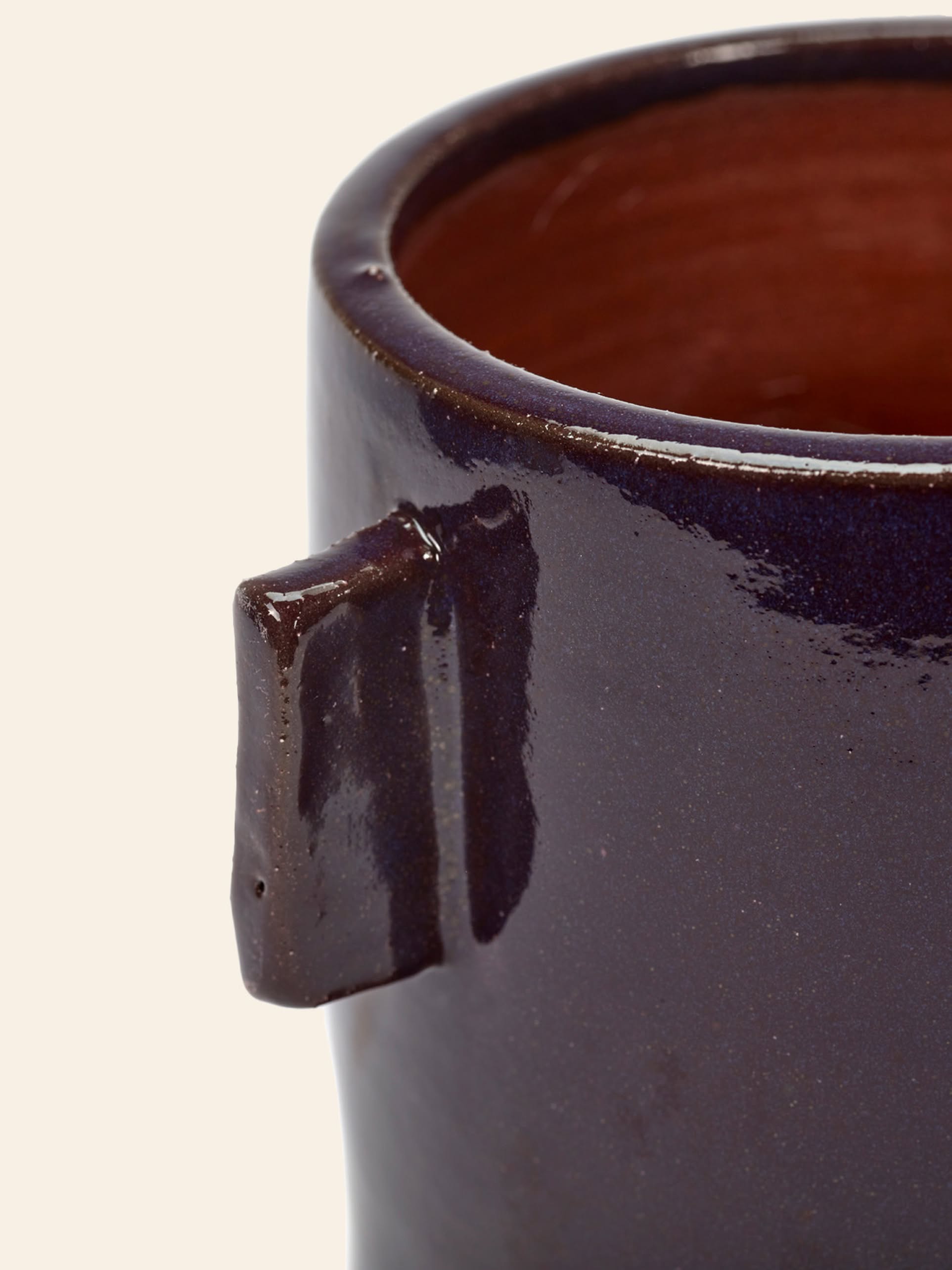 Close-up of the Serax Urban Jungle Glazed Flower Pot M in aubergine, featuring a rectangular handle and glossy, waterproof finish with a brown interior. This Serax pot is partially visible against a light background, perfect for brightening indoor spaces.