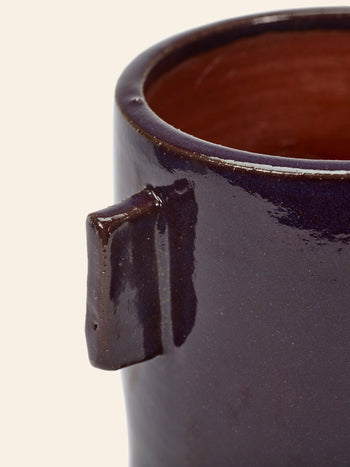 Close-up of the Serax Urban Jungle Glazed Flower Pot M in aubergine, featuring a rectangular handle and glossy, waterproof finish with a brown interior. This Serax pot is partially visible against a light background, perfect for brightening indoor spaces.