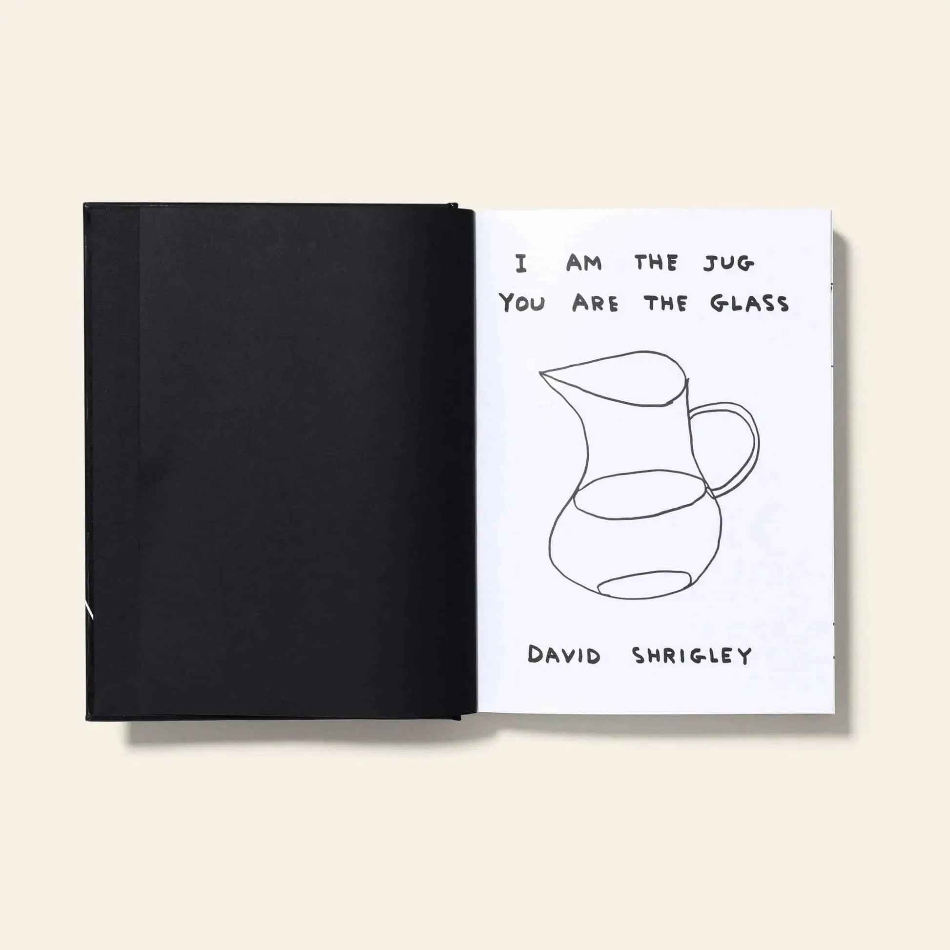An open Shrig Shop David Shrigley – I Am The Jug You Are The Glass book shows a black blank page on the left and, on the right, a sketch of a jug with the handwritten text “I AM THE JUG YOU ARE THE GLASS” above it.